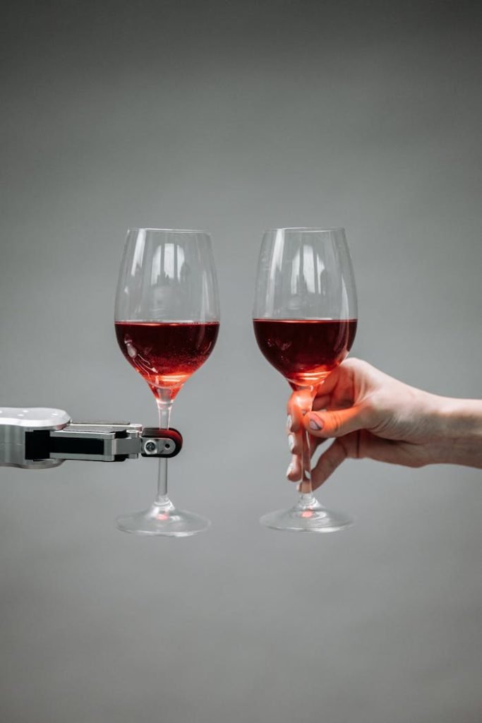 A robotic arm and human hand toasting with red wine glasses, symbolizing human-robot interaction.